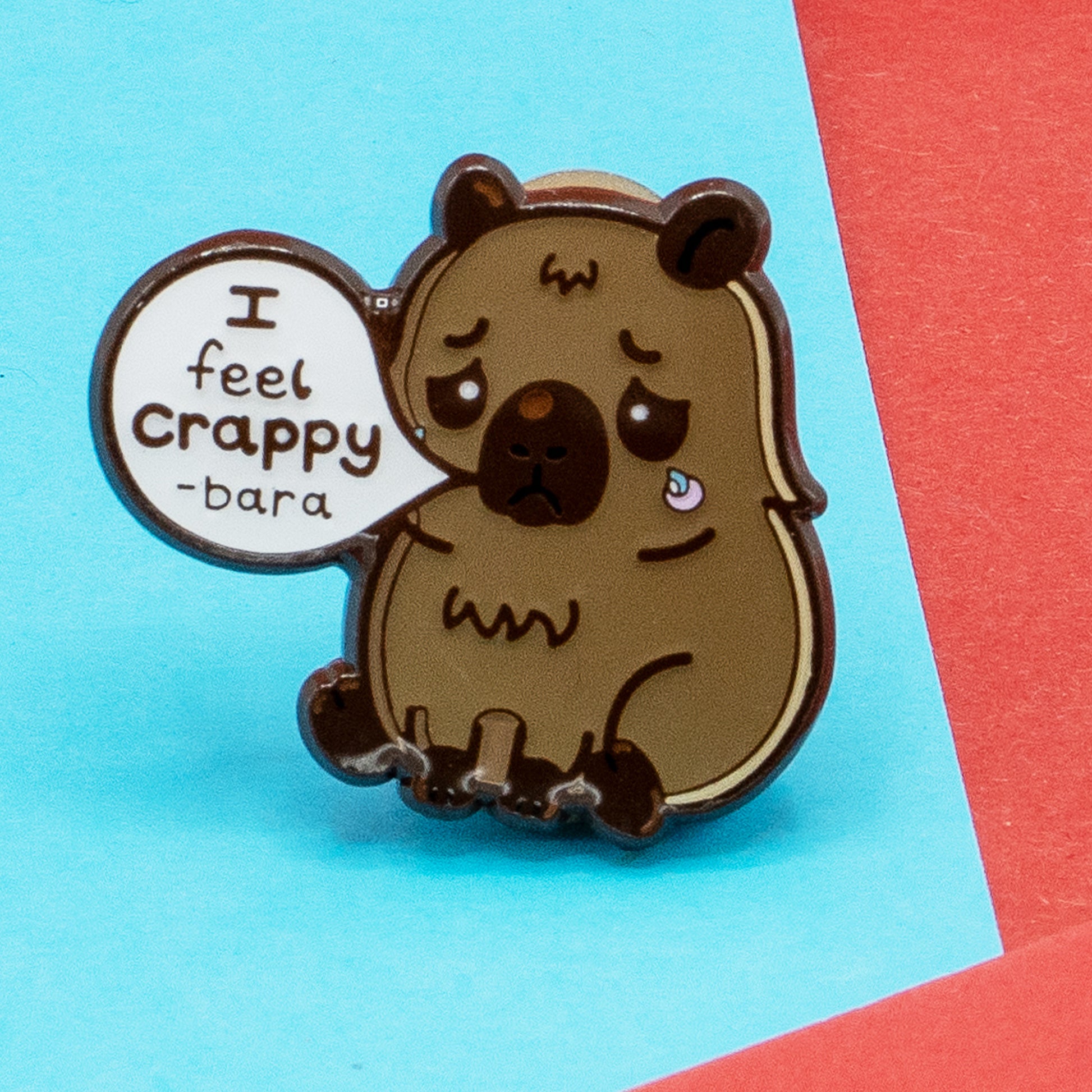 Close-up of Innabox I Feel Crappy-Bara enamel pin, showing a sad kawaii capybara with a tear and speech bubble that reads “I feel crappy-bara”. Gentle, disability-inspired design to support awareness of depression, chronic illness, and hidden disabilities.
