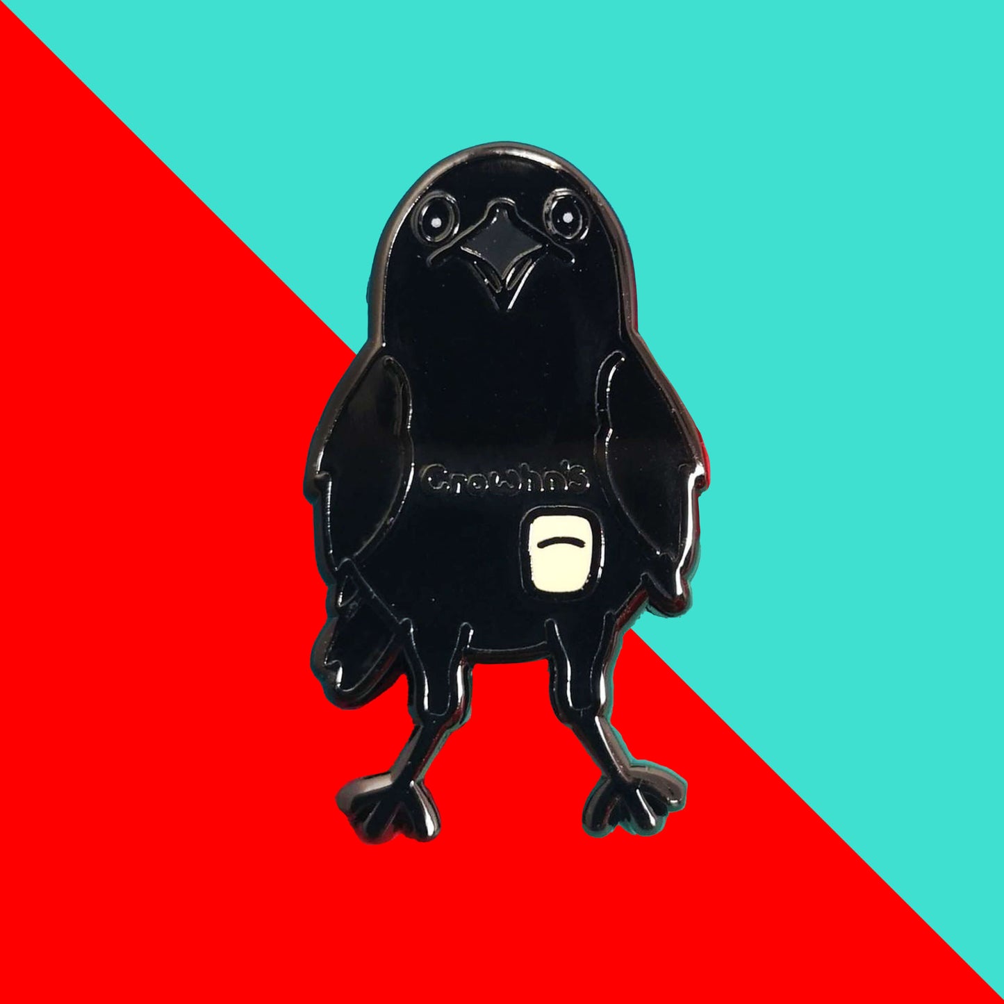 The Crowhn's Disease Enamel Pin - Crohn's Disease on a red and blue background. The black crow shape pin has a white stoma bag fitted and the text reading 'chrowhn's' across its chest. The design is raising awareness for crohn's disease.
