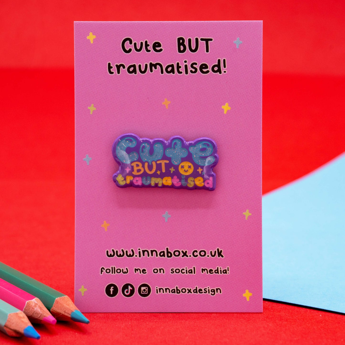Cute But Traumatised glitter enamel pin by Innabox displayed on a pink backing card with colourful stars. A supportive and uplifting accessory designed to raise awareness for hidden disabilities and chronic illness.