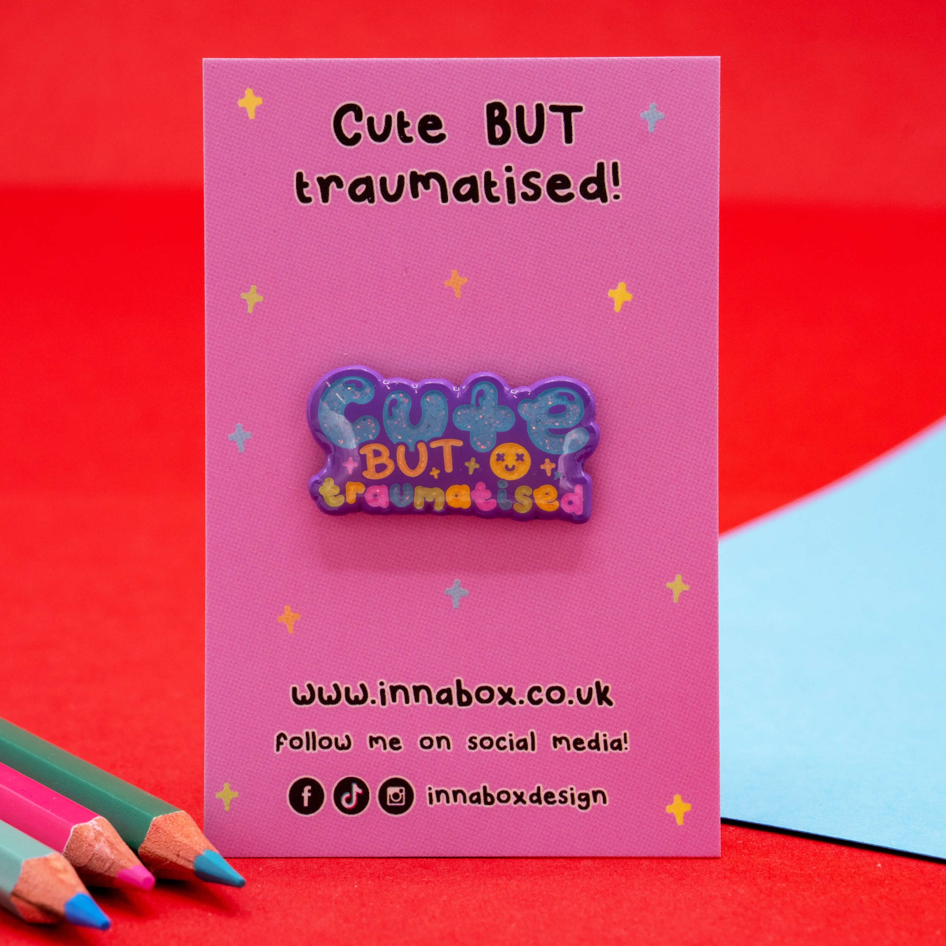 Cute But Traumatised glitter enamel pin by Innabox displayed on a pink backing card with colourful stars. A supportive and uplifting accessory designed to raise awareness for hidden disabilities and chronic illness.