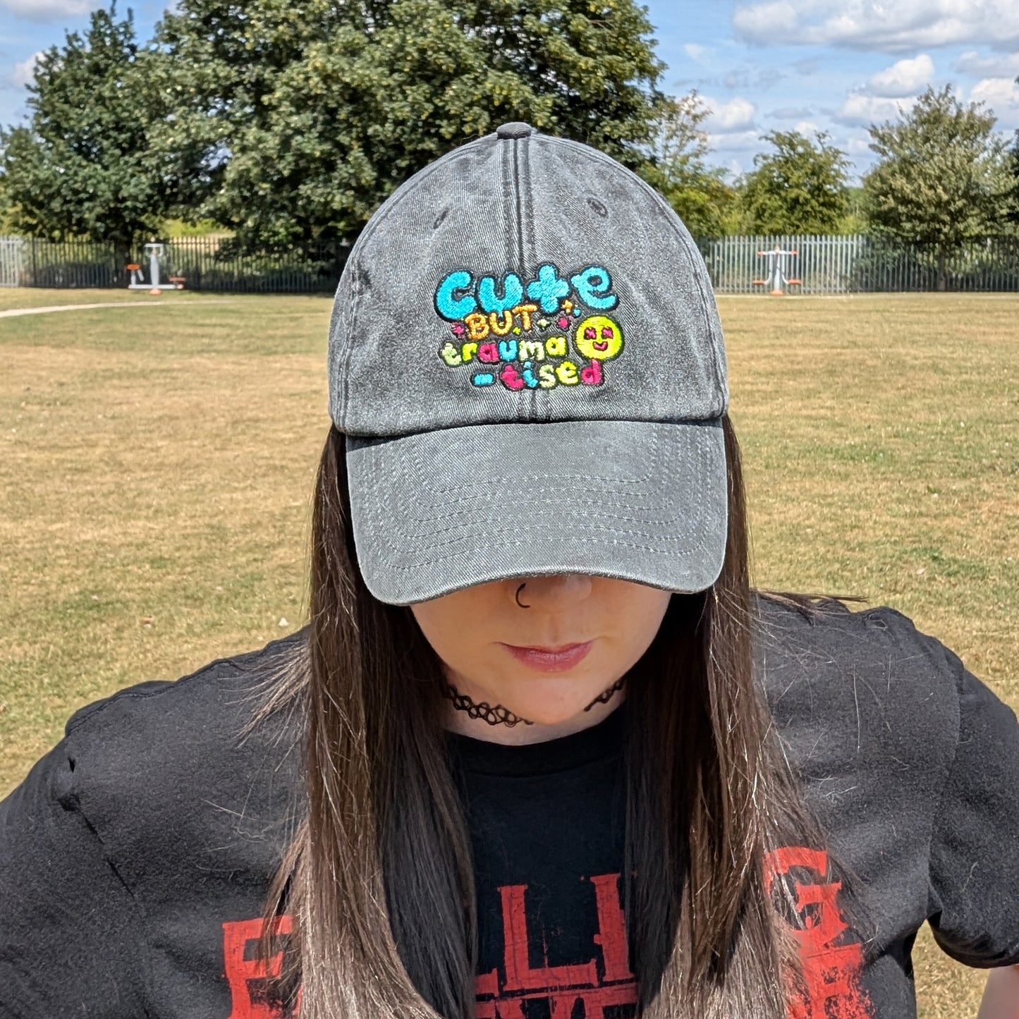 Front-facing shot of a model wearing the Hot and Neuro-Spicy cap in a grassy park, clearly showing the bright embroidery and vintage washed fabric in natural daylight.