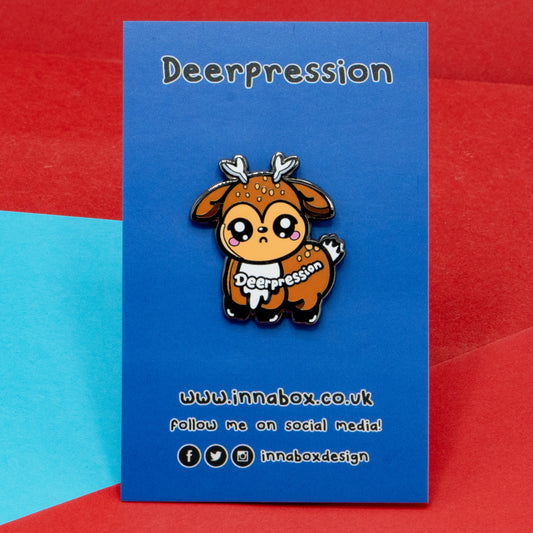 Innabox Deerpression 2.0 enamel pin displayed on a branded backing card with blue background. Features a cute deer character with antlers, sad eyes and blushing cheeks, with the word "Deerpression" on its side. Disability-inspired pin supporting mental health and chronic illness awareness.