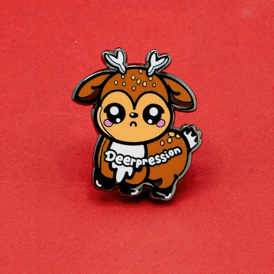 Deerpression 2.0 enamel pin by Innabox, showing a kawaii-style deer with antlers, big shiny eyes, and pink cheeks. The word "Deerpression" is written across the character. A gentle, uplifting pin made to raise awareness around depression and hidden disabilities.