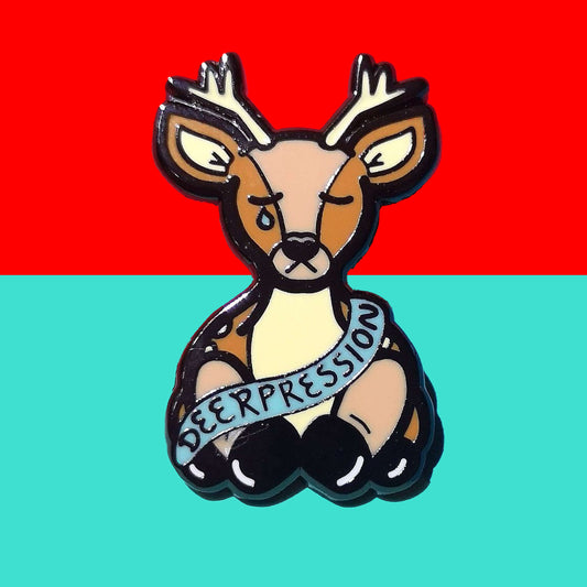 The Deerpression Enamel Pin - Depression on a red and blue background. The deer shape pin its eyes closed with a blue tear falling from one eye, across its front is a blue banner with black text reading 'deerpression'. The design was created to raise awareness for depression.