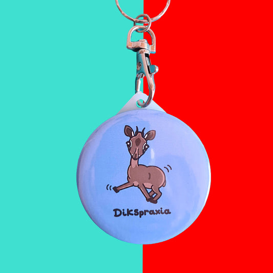 The Dikspraxia Keyring - Dyspraxia on a red and blue background. The plastic pastel blue circular keychain with silver metal lobster clip features a brown dik dik antelope with its two front legs splayed out chaotically with movement lines either side, below in black reads 'dikspraxia'. The design is raising awareness for dyspraxia and neurodivergence.