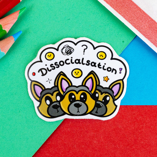 Dissocialsation Sticker - Dissociation on a blue, green and red background with a red stripe candy bag and colouring pencils. Three confused brown and black Alsatian dog heads with their ears perked up, above them is a white cloud with sad and happy yellow faces, sparkles, question marks and black text reading 'dissocialsation!'. The design is raising awareness for dissociation.