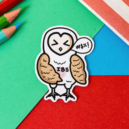 The Irritable Owl Syndrome Sticker - Irritable Bowel Syndrome (IBS) on a red, blue and green background with colouring pencils and a red stripe candy bag. The barn owl sticker has its eyes shut with a wing on it's swirling red belly and a speech bubble with swearing symbols inside, across its middle in black text reads 'IBS'. The hand drawn design is raising awareness for irritable bowel syndrome and food intolerances.