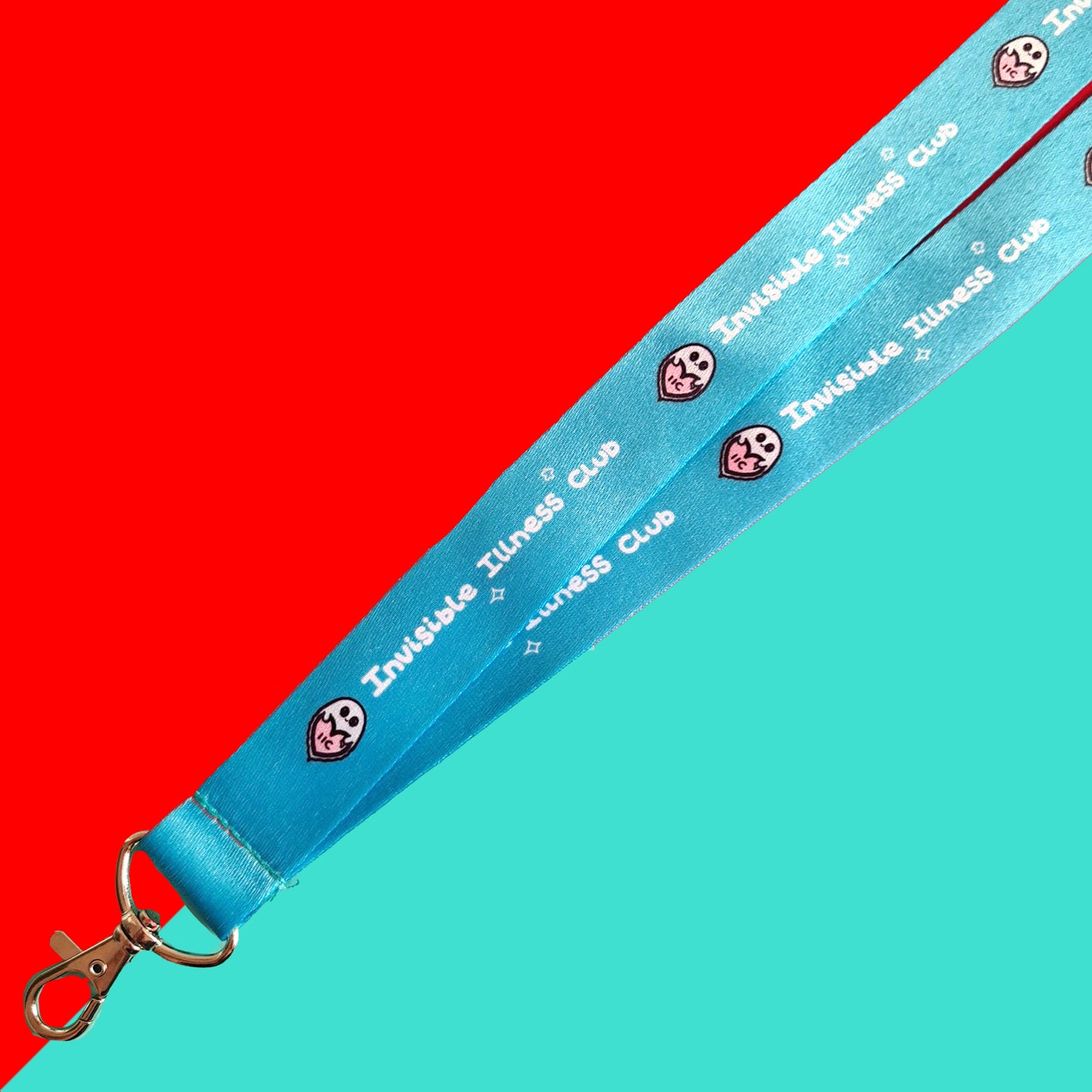 The Invisible Illness Club Lanyard on a red and blue background. The pastel blue lanyard has repeating white text reading 'invisible illness club' and innabox pastel ghost logo. It has a silver lobster clip and white safety break. The hand drawn design is raising awareness for hidden disabilities.