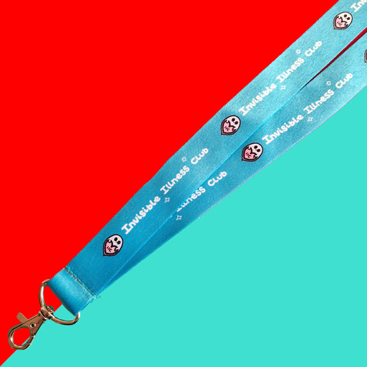 The Invisible Illness Club Lanyard on a red and blue background. The pastel blue lanyard has repeating white text reading 'invisible illness club' and innabox pastel ghost logo. It has a silver lobster clip and white safety break. The hand drawn design is raising awareness for hidden disabilities.