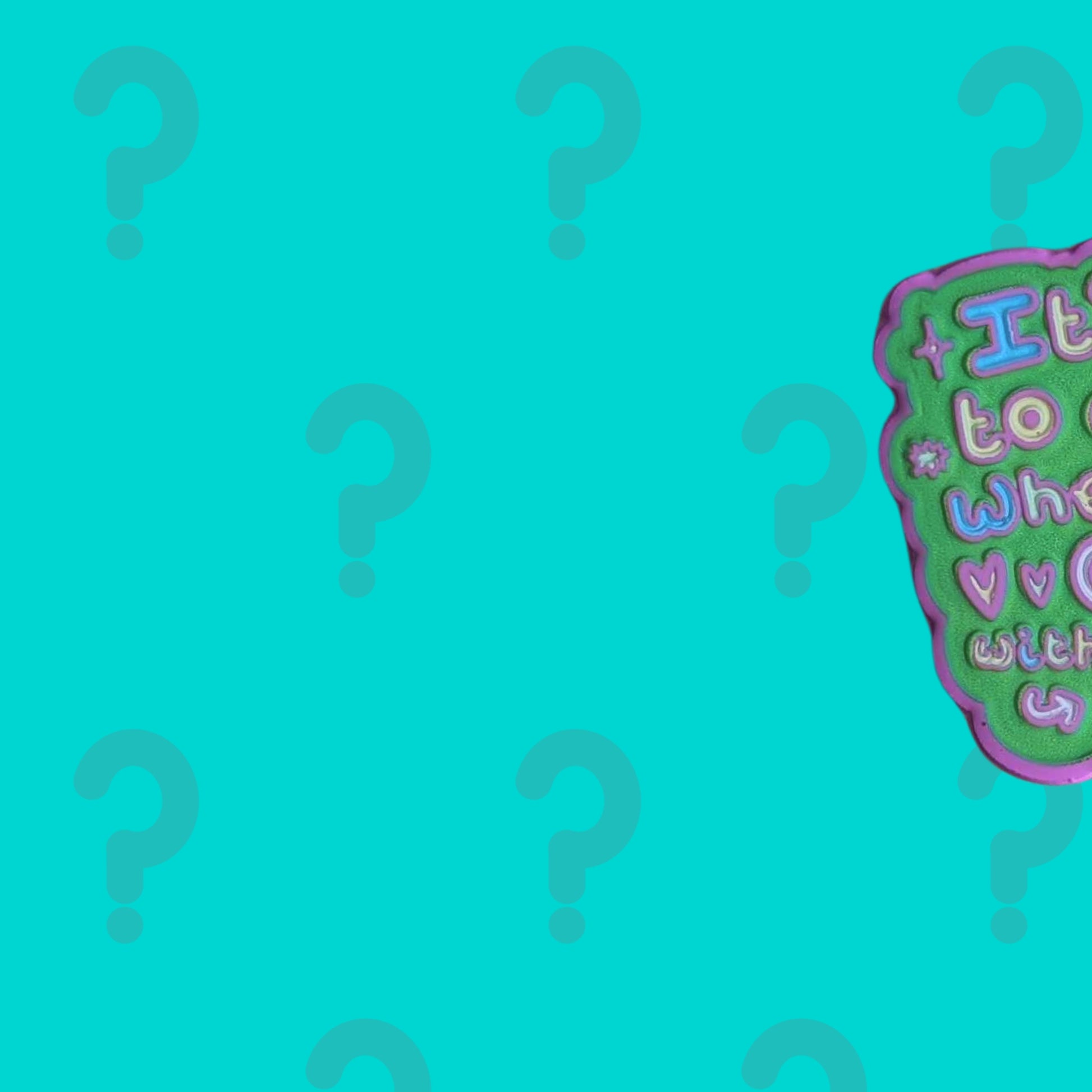 Partial reveal of Innabox March Theme Exclusive Mystery Enamel Pin with colourful raised lettering and playful design details against a teal question mark background. Monthly enamel pin subscription celebrating disability awareness, chronic illness visibility and hidden disabilities.
