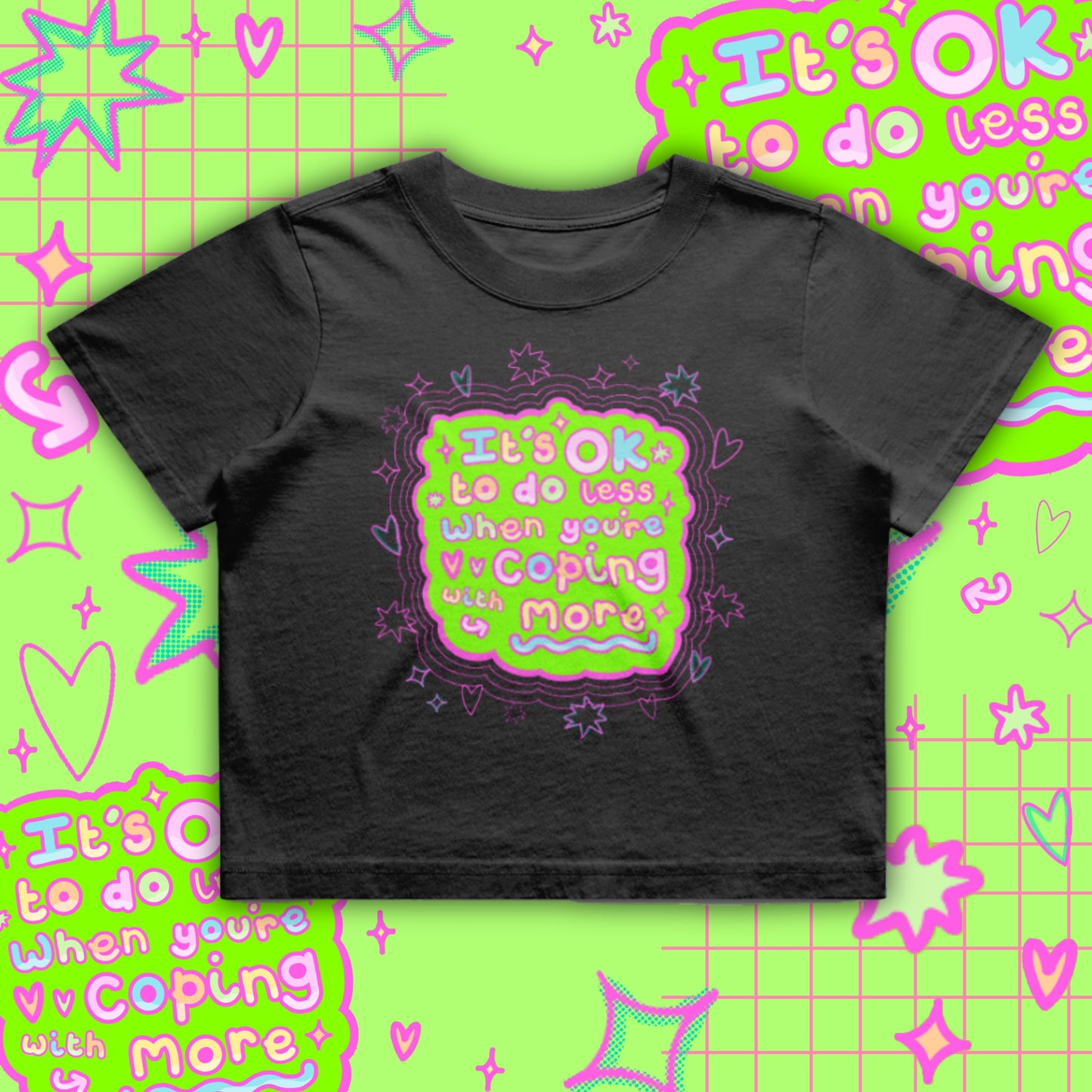 Black cropped t-shirt by Innabox featuring a bright neon green and pink graphic reading “It’s OK to do less when you’re coping with more”. Boxy oversized fit with a soft cotton finish. Disability awareness clothing designed to support people with chronic illness, mental health struggles and hidden disabilities.