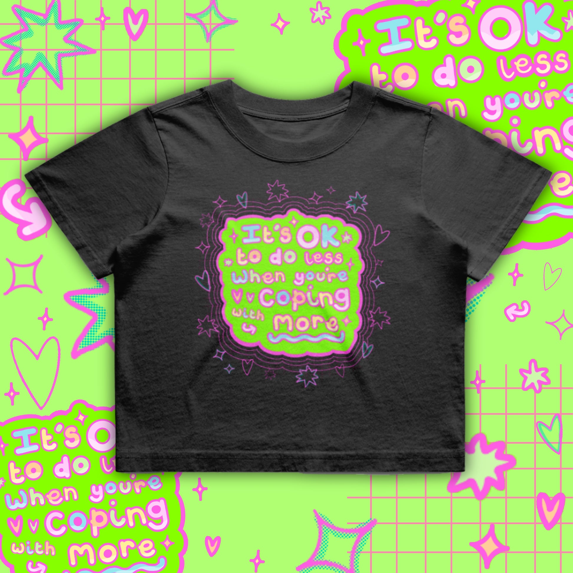 Black cropped t-shirt by Innabox featuring a bright neon green and pink graphic reading “It’s OK to do less when you’re coping with more”. Boxy oversized fit with a soft cotton finish. Disability awareness clothing designed to support people with chronic illness, mental health struggles and hidden disabilities.