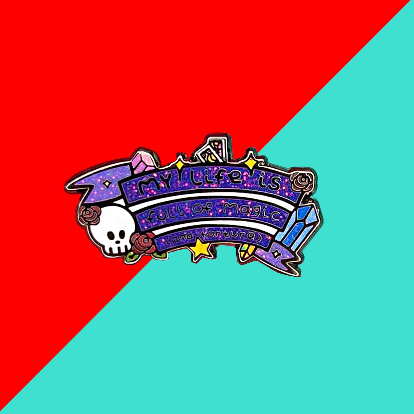The My Life is Full of Magic & Torture Glitter Enamel Pin on a red and blue background. The glittery finish enamel pin badge features a purple banner sash of black text reading 'my life is full of magic (and torture)' with yellow sparkles, crystals, red roses, tarot cards and a skull head.