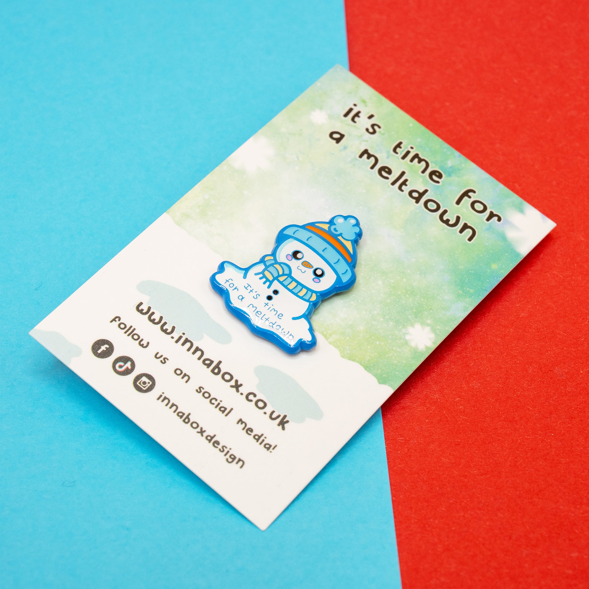 A front facing view of the Innabox ‘It’s Time For A Meltdown’ Snowman Enamel Pin attached to its snowy themed backing card. The cute blue snowman illustration and comforting message make this 30mm enamel pin a thoughtful gift for anyone managing chronic illness, overwhelm or hidden disabilities.