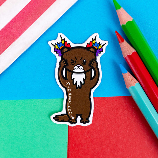 Misophonia sticker on a red and blue background. The sticker is in the shape of a mink standing on it's back legs with it's hands holding it's face. The mink is a brown colour with white fluffy chest and mouth. It has one eye shut and upward angled eyebrows with multi-coloured lightening bolt shapes coming out of it's little ears. Down the side of it's body reads 'minksophonia' in white letters.