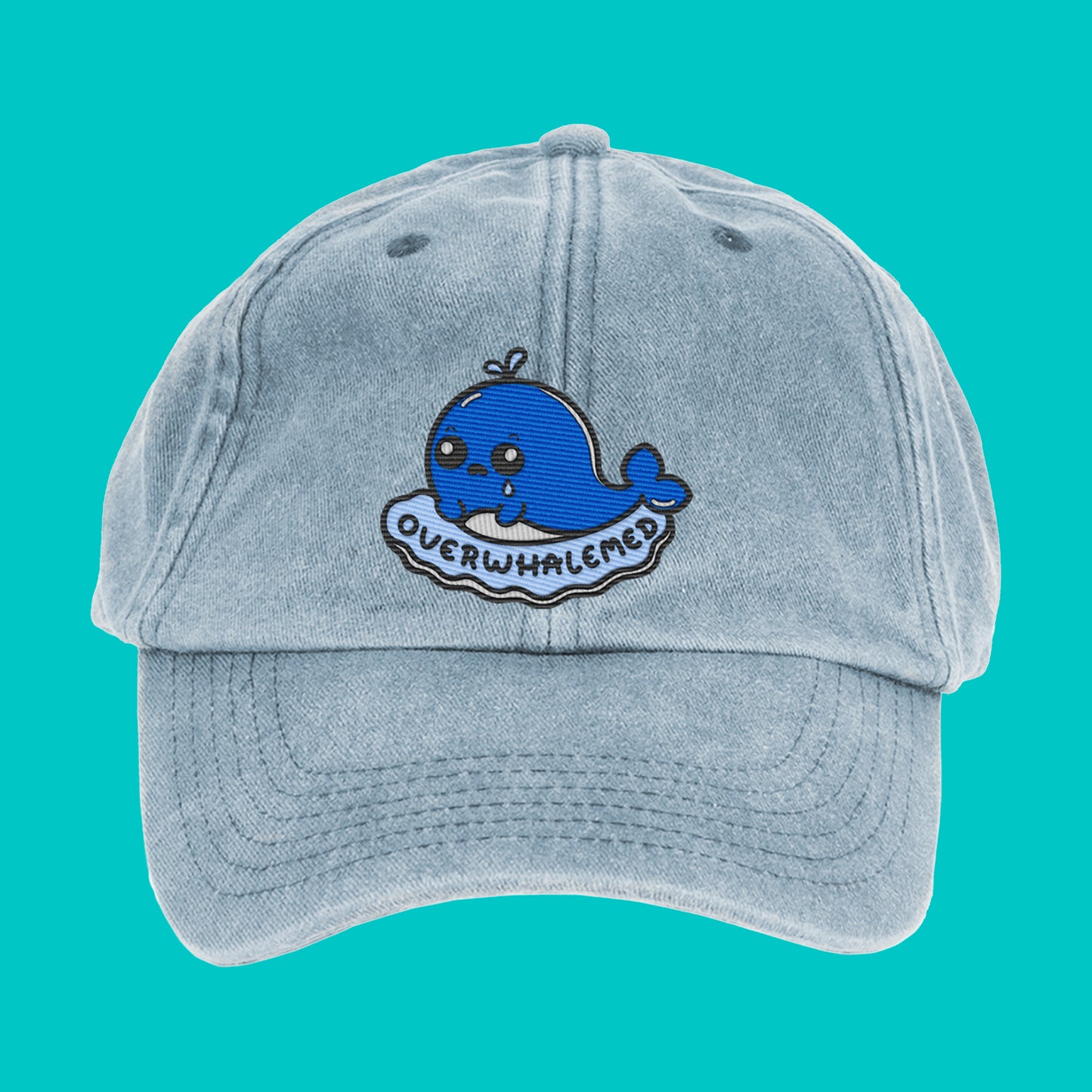 Light blue vintage denim cap featuring a cute embroidered blue whale with sad eyes and the text “Overwhalemed.” Disability-inspired design by Innabox.