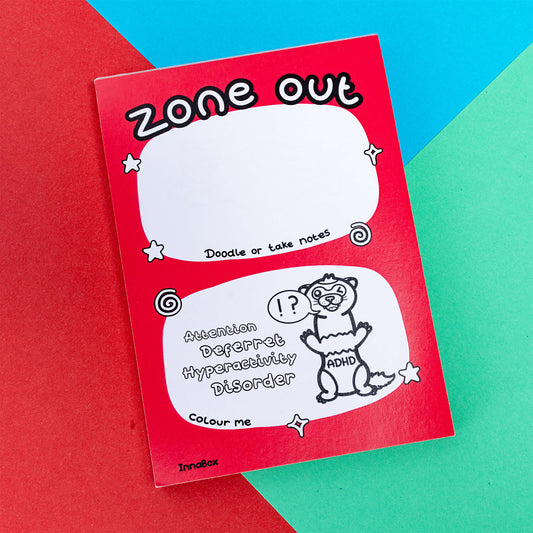 A zone out notebook with a ferret with ADHD written on its tummy and the words 'Zone out' on the top it is on a blue, green and red background. A hand drawn design to raise awareness for neurodiversity, adhd, autism.
