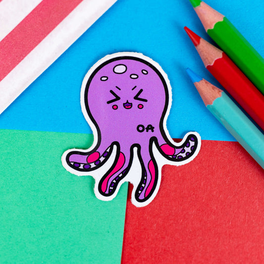 The Octeoarthritis Octopus Sticker - Osteoarthritis on a red, blue and green background with colouring pencils and red stripe candy bag. The purple smiling octopus has red patches all over its tentacles with the black intials 'OA' on its body. The hand drawn design is raising awareness for Osteoarthritis.