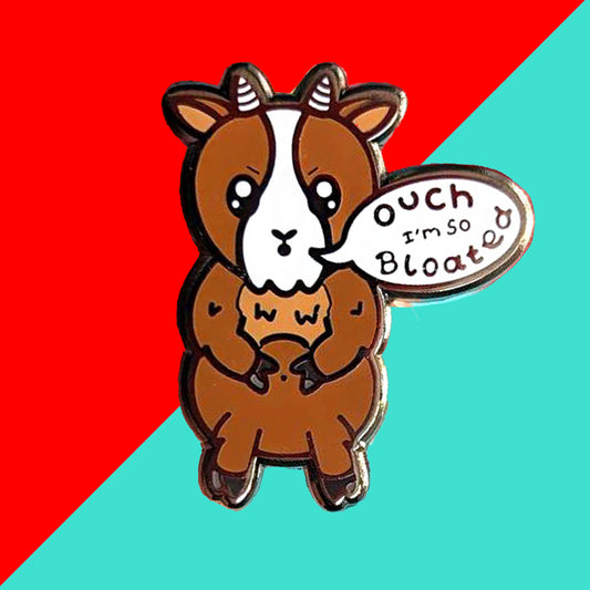 The Bloat Goat Enamel Pin on a red and blue background. The brown frustrated goat pin badge is stood up clutching its tummy with a speech bubble reading 'ouch I'm so bloated'. The hand drawn design is raising awareness for chronic illnesses or hidden disabilities that cause bloating.