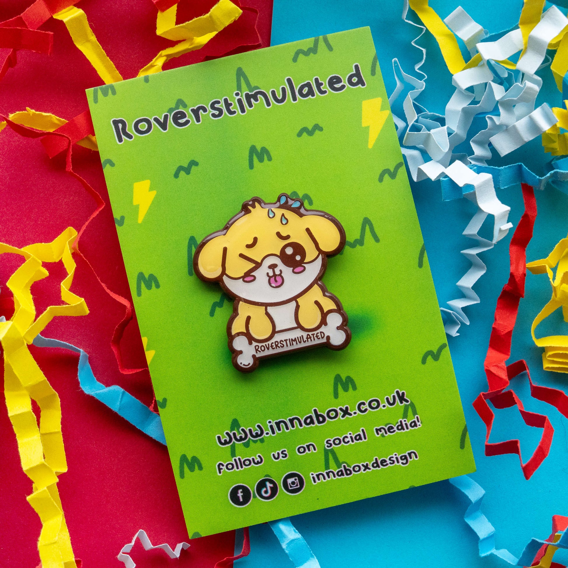 Roverstimulated Dog hard enamel pin by Innabox on branded green display card with social media details. Cute yellow dog character with glossy detailing and “Roverstimulated” bone text. Disability inspired pin supporting chronic illness and hidden disability awareness.
