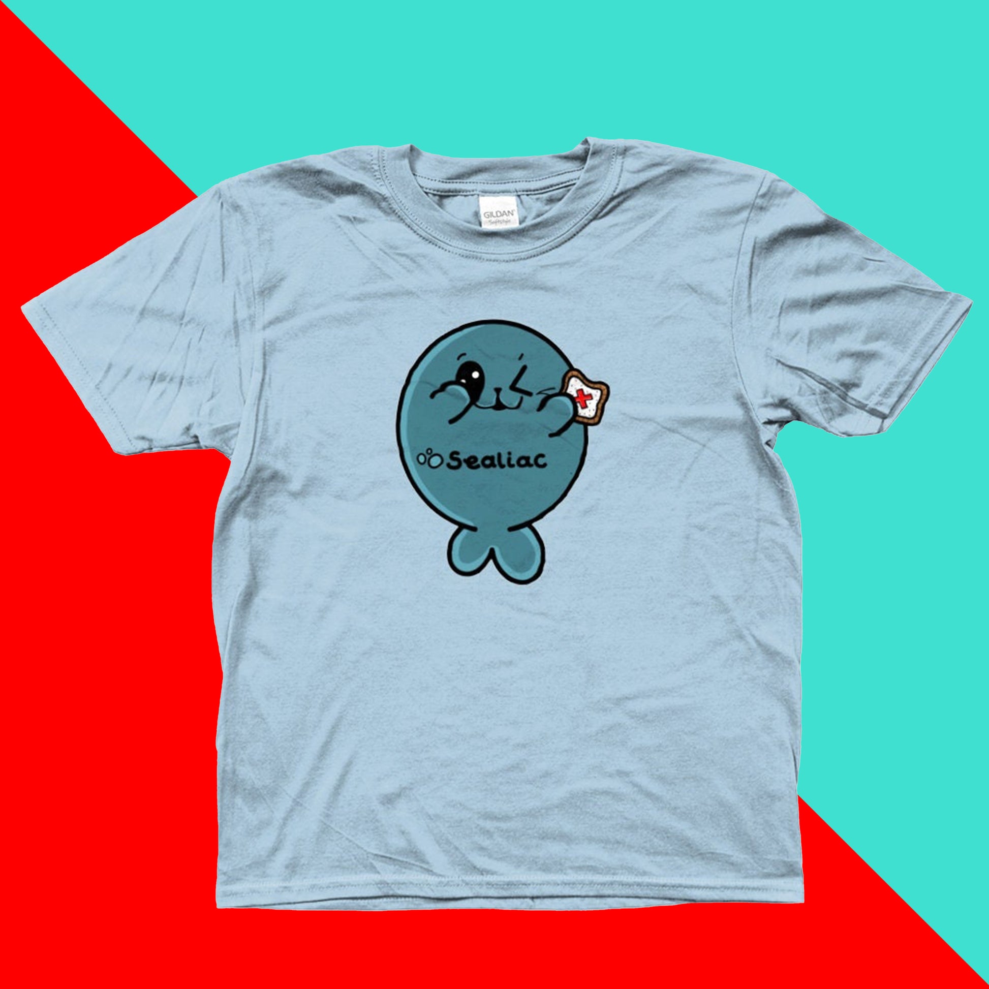 The Sealiac Coeliac Kids Tee - Coeliac on a red and blue background. The light blue short sleeve tshirt features a winking blue seal holding up a piece of toast with a red cross in the middle, across its belly in black reads 'Sealiac'. The hand drawn design is raising awareness for Coeliac and gluten allergy.