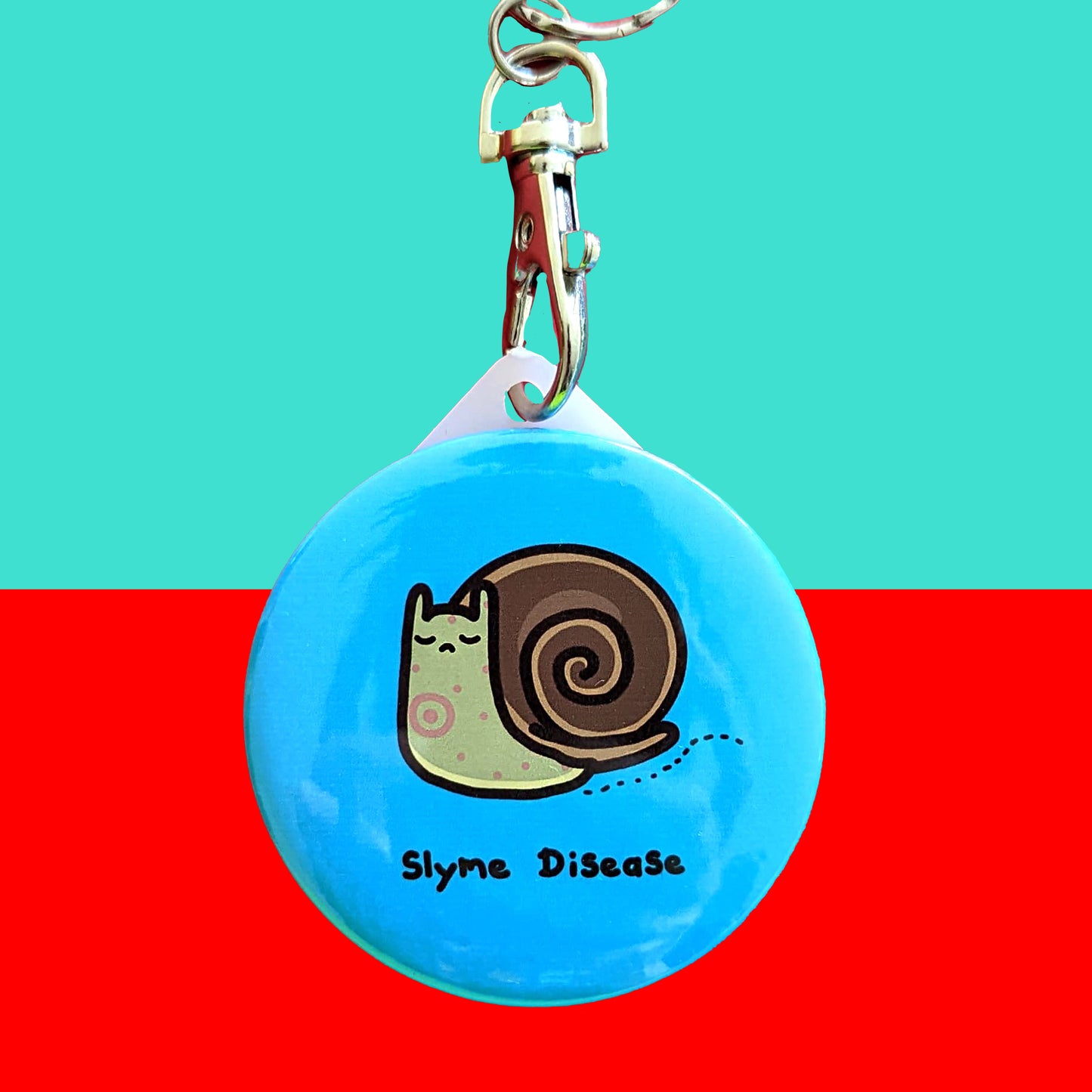Slyme Disease Snail Keyring - Lyme Disease on a red and blue background. The pastel blue plastic circular keychain with silver lobster clip features a sad brown snail with red spots, underneath is black text reading 'slyme disease'. The hand drawn design is raising awareness for lyme disease.