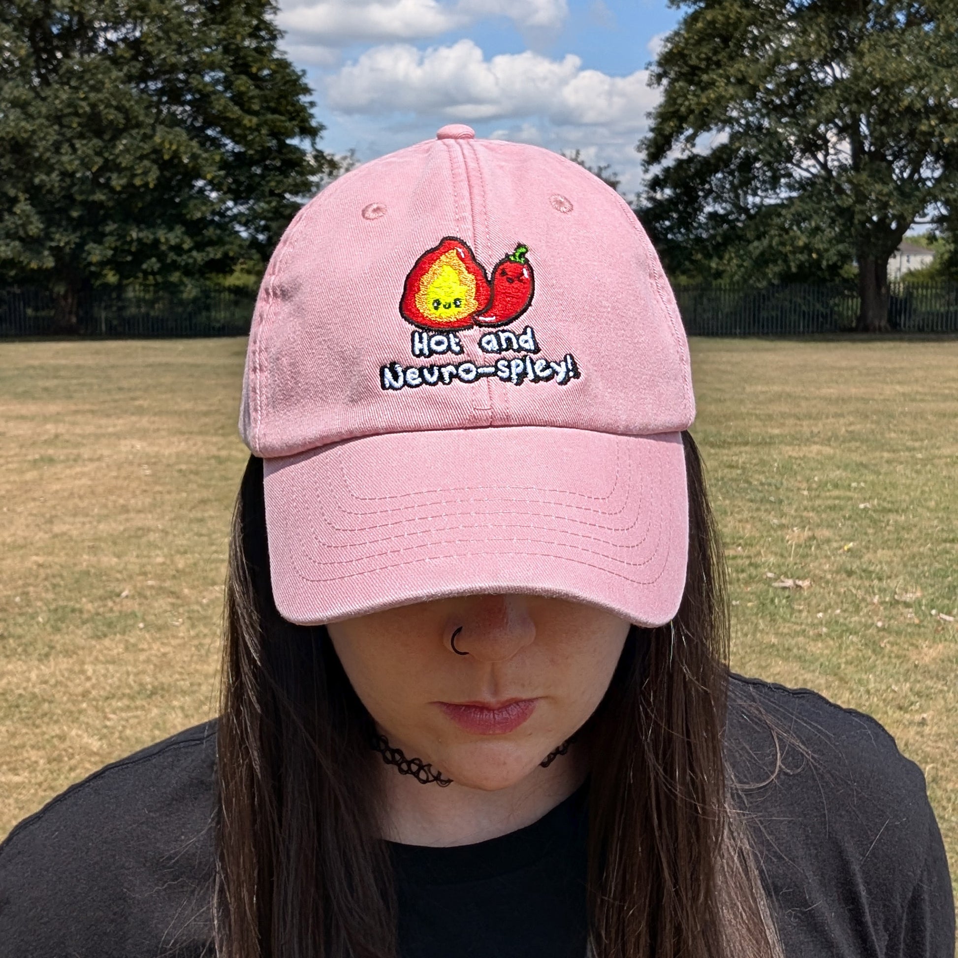 Front-facing view of a person modelling the Hot and Neuro-Spicy cap by Innabox. Pink cotton cap with embroidered spicy design celebrating neurodiversity.