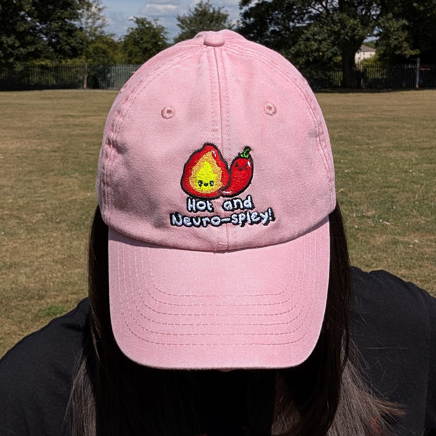Person looking down while wearing the pink Hot and Neuro-Spicy cap by Innabox. Embroidered design visible with flame and chilli character promoting neurodivergent pride.