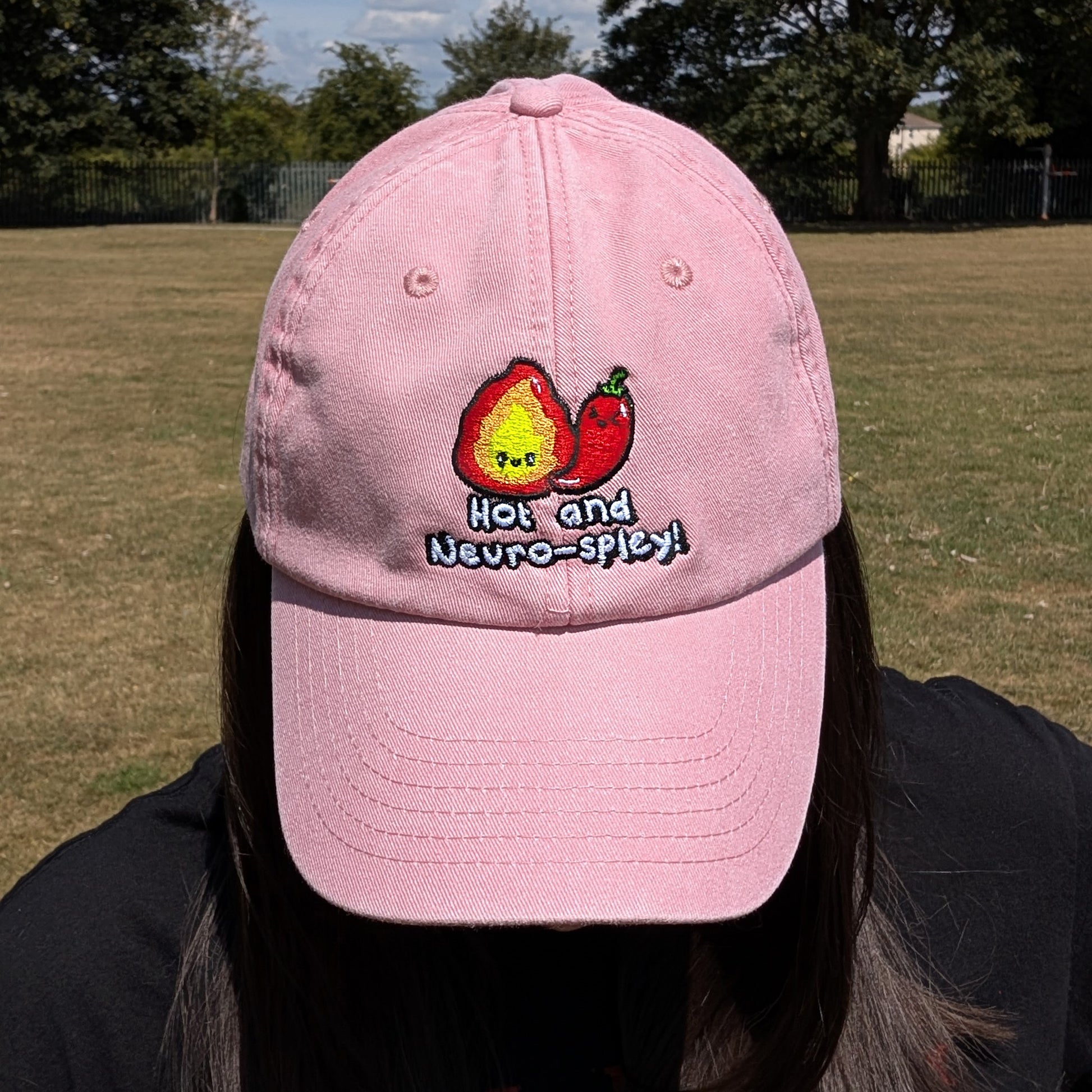 Person looking down while wearing the pink Hot and Neuro-Spicy cap by Innabox. Embroidered design visible with flame and chilli character promoting neurodivergent pride.