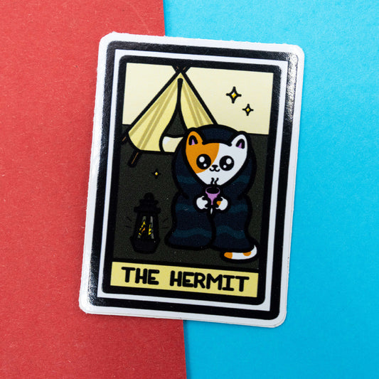 Cute Hermit tarot cat sticker by Innabox featuring a calico cat in a cloak holding a cup, with a lantern and tent in the background.