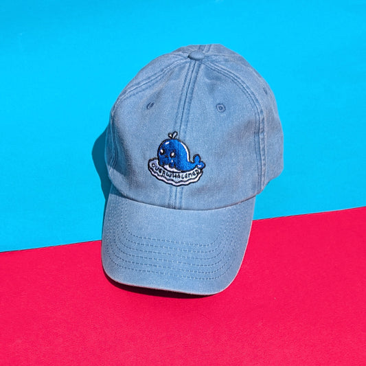 Full view of the Innabox Overwhalemed cap on a bright flat lay background. Light blue vintage-style cotton cap with emotional support whale patch.