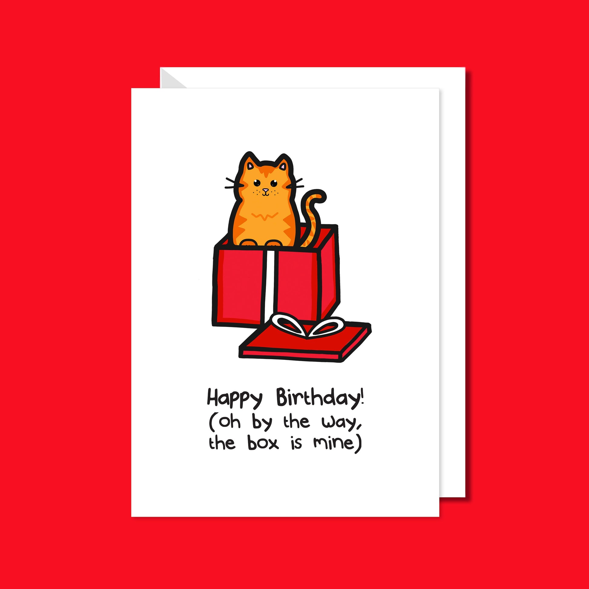 A white card with a ginger cat illustration coming out of a red present with text saying Happy Birthday! (Oh by the way, the box is mine). The a6 birthday card on a red background with a white envelope underneath.
