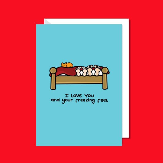 I love You And Your Freezing Feet Card on a red background. the light blue card has an illustration of a wooden bed with two pairs of feet poking out from under the red blanket and a ginger cat sat on top of it